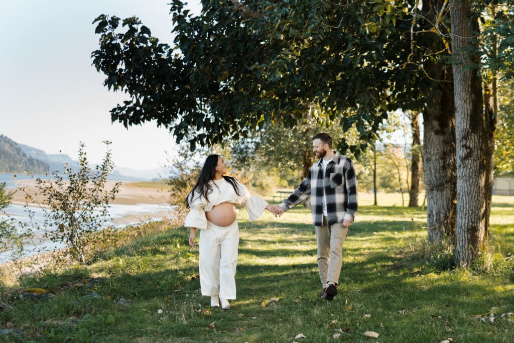 pregnant woman and man holding hands in a park by the river